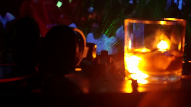 詳情圖-在夜總會(huì)的dj控制器上，裝有冰塊的威士忌酒杯。在迪斯科燈光下的夜總會(huì)音樂派對上，一杯威士忌上戴著Dj耳機(jī)。滑塊拍攝