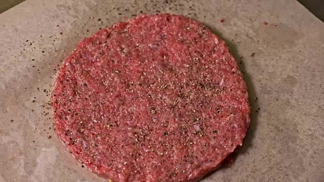 厨师为汉堡制作肉奖章。戴着黑色食品手套的厨师做肉排。在一个均匀的大奖章上，排骨被平放在钢环中。肉放在食物纸上，用保鲜膜包起来。