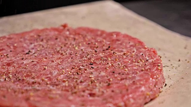厨师为汉堡制作肉奖章。戴着黑色食品手套的厨师做肉排。在一个均匀的大奖章上，排骨被平放在钢环中。肉放在食物纸上，用保鲜膜包起来。