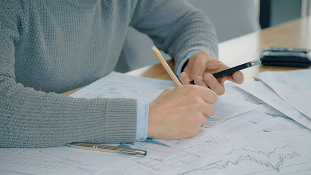 男性的手在办公室用智能手机检查图表值的特写