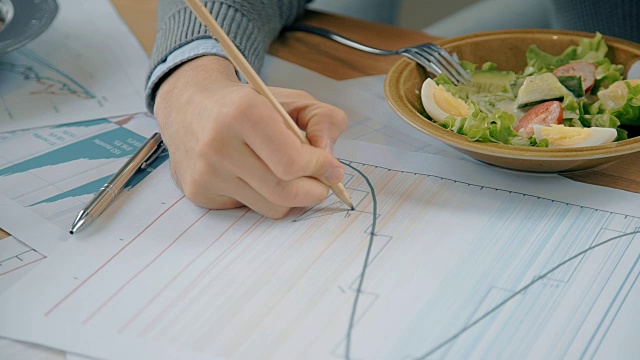 近手男性金融分析绘图倾向在纸图表上的咖啡厅