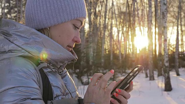 一个女人走在树林里。旅行者在森林里用手机拍照。女孩会自拍，用智能手机交流。美丽多汁的日落时分。