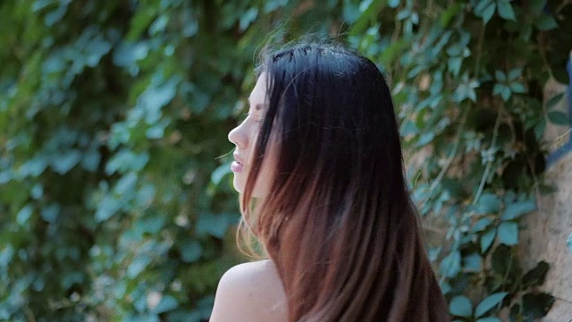 詳情圖-肖像的年輕迷人的女孩轉(zhuǎn)身和看著鏡頭微笑。東方面孔，棕色眼睛和時(shí)尚的深褐色長發(fā)染在樹葉的背景