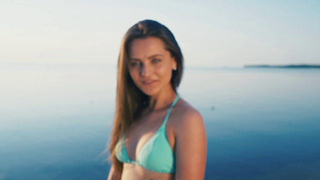 详情图-海滩上快乐的年轻女子。女游客穿着比基尼在假期对着镜头做和平手势