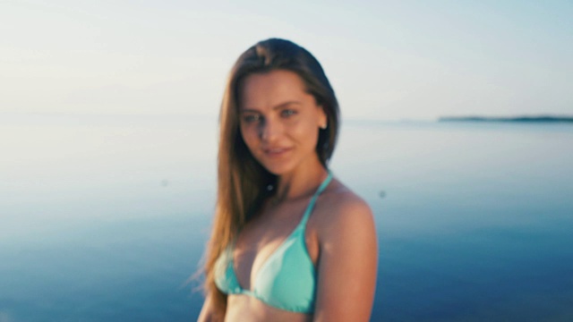 详情图-海滩上快乐的年轻女子。女游客穿着比基尼在假期对着镜头做和平手势
