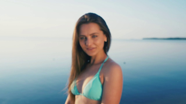 详情图-海滩上快乐的年轻女子。女游客穿着比基尼在假期对着镜头做和平手势