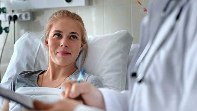 詳情圖-男醫(yī)生在病床上與女病人交談。微笑的醫(yī)生與剪貼板和x光照片主治女病人在醫(yī)院病房