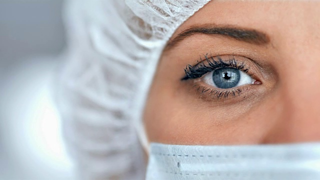 在医院或实验室里戴着外科口罩，背景模糊的医护人员或科学家