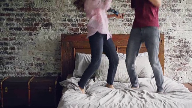 詳情圖-好玩的年輕人男人和女人在床上跳舞聽音樂和唱歌用吹風(fēng)機和電視遙控器作為麥克風(fēng)一起玩。