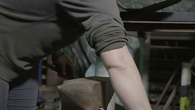 近距离的妇女铁匠锤一根金属杆，以使其在她的diy车间使用不同的锤子