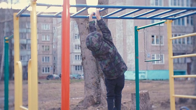 一个男孩在城市房子院子里的单杠上爬。在操场上做游戏和散步。