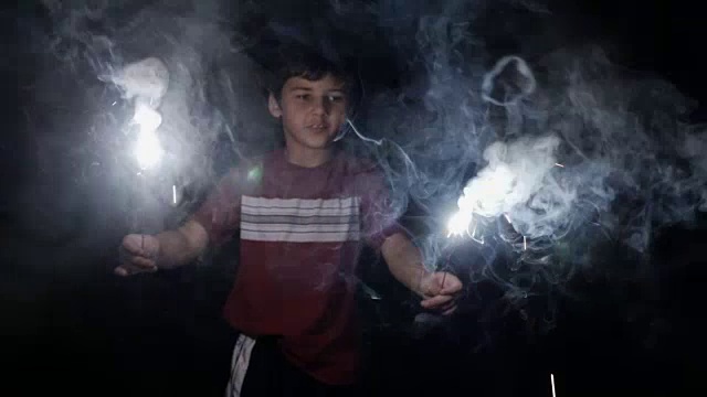 有吸引力的年轻8 - 10岁的男孩拿着两个燃烧的烟花和烟花