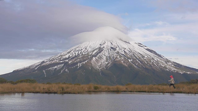 慢镜头——旅行者漫步到新西兰北岛的塔拉纳基火山的景色中，在湖中看到山和攀登者的倒影。新西兰被