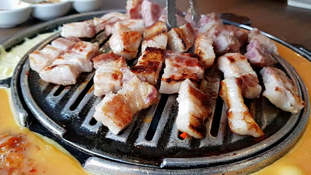 将猪肉切片放在平底锅和夹钳上烤和烧烤。平底锅的一边有煎蛋卷和奶酪。韩国烤肉(烧烤)