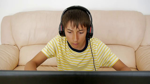 青少年使用笔记本电脑。沉迷于视频游戏的青少年用耳机粘在笔记本屏幕上按键盘。