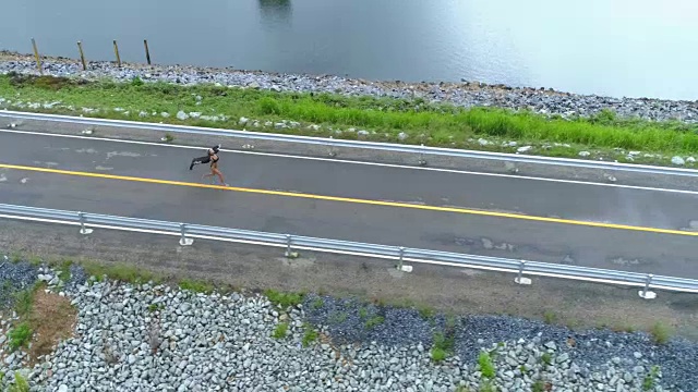 航拍:一个美丽的女孩沿着公路跑在大坝上。