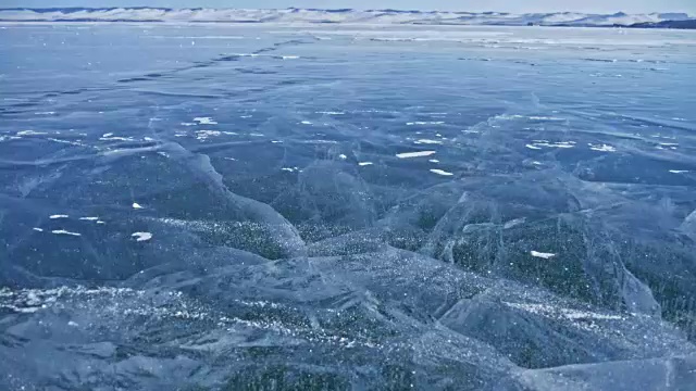 雪在冰面上飞舞。雪花在贝加尔湖的冰面上飞舞。冰非常美丽，有独特的裂缝。背景视图山景。雪花闪耀着红光。