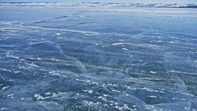 詳情圖-雪在冰面上飛舞。雪花在貝加爾湖的冰面上飛舞。冰非常美麗，有獨特的裂縫。背景視圖山景。雪花閃耀著紅光。