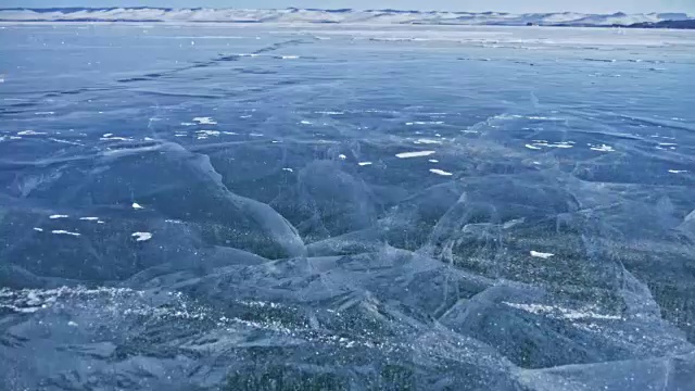 詳情圖-雪在冰面上飛舞。雪花在貝加爾湖的冰面上飛舞。冰非常美麗，有獨特的裂縫。背景視圖山景。雪花閃耀著紅光。