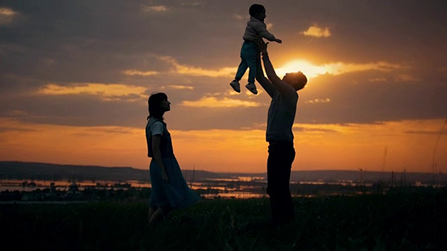 父母把他的儿子抛向空中，一个夏日的黄昏，夕阳