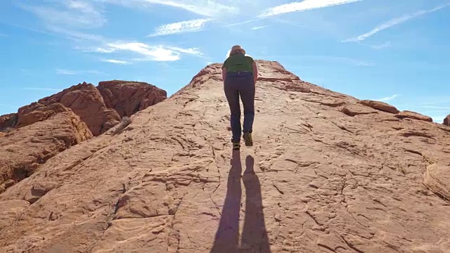 一个女人爬上巨大的红色岩石上的山