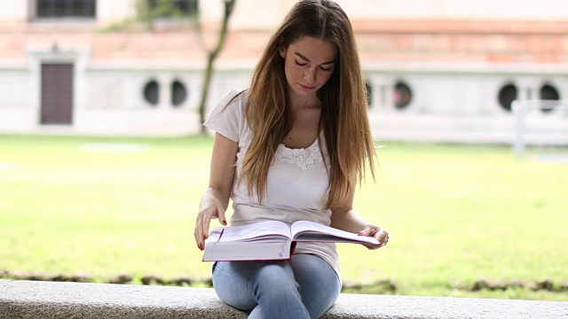 美丽的女大学生在公园的长椅上看书