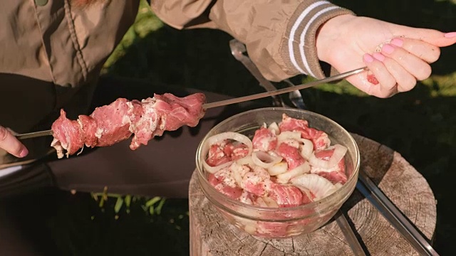 年轻女子把肉串起来。特写镜头。做烤肉串。