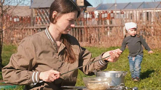 年轻女子把肉串起来。做烤肉串。她的女儿到处走动。