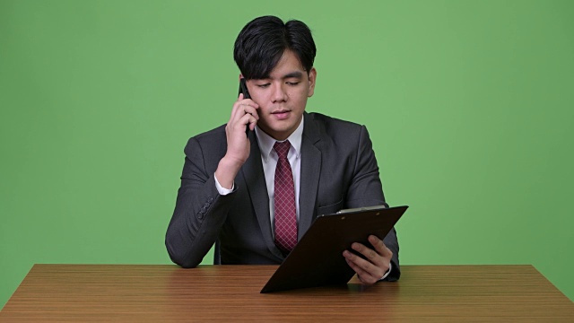 年轻英俊的亚洲商人与剪贴板在绿色背景下工作