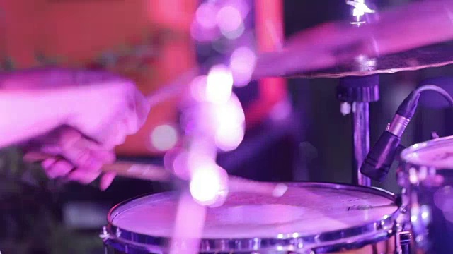 音乐家不知名的鼓手打鼓与鼓槌在音乐会派对在夜总会的慢镜头近距离。男子在舞台上用棍棒打鼓现场表演，彩色灯光手背侧视