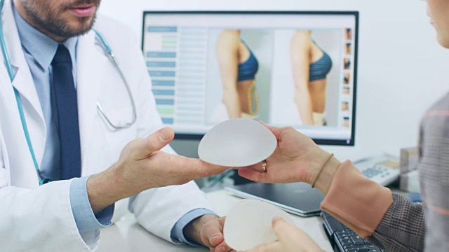 整形/整容外科医生为她的未来手术展示女性患者乳房植入样本。专业、著名的外科医生在体面的诊所工作。