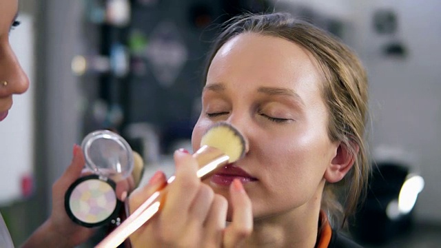 化妆师用闪亮的阴影来修饰妆容。用手指和刷子涂在脸上、鼻子上。工作室。近距离