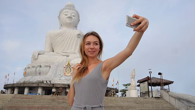 慢动作模特年轻女子在泰国佛像附近用智能手机自拍