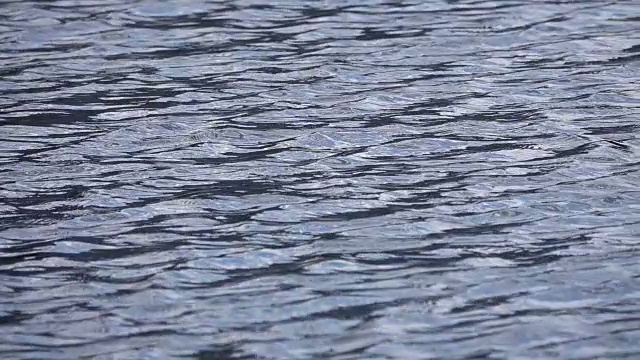 在蓝天白云的映照下，深蓝色的水面上泛起涟漪的慢镜头。