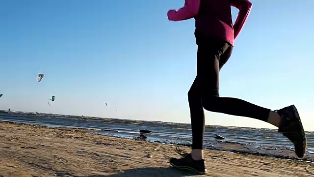 年轻女子在夏天跑在海边，背景是风筝冲浪者。日落时分，女孩在沙滩上跑步，慢镜头