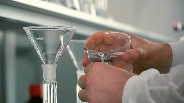 药剂师通过漏斗将液体倒入烧瓶中