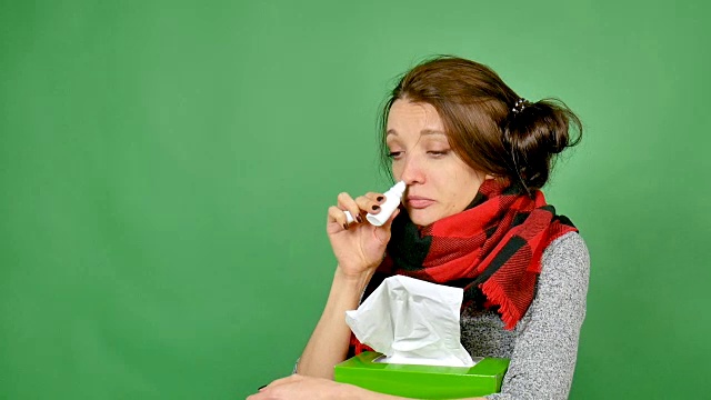 一个漂亮的患流感的黑发女人的肖像。那个女孩感冒了，发烧了，脖子上裹着围巾。她挖鼻子用滴鼻药水