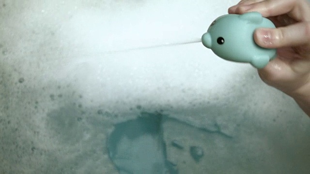 详情图-一个白人小男孩在他的浴缸里玩耍和清洁，而他的妈妈用一个玩具喷射他