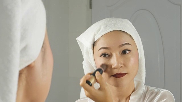 漂亮的女人看着镜子，涂着腮红