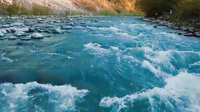 低空飞过奔流的山河，和晶莹的绿松石之间的山脉。在背景中，游客们被拍照。日落时间。太阳光发出橙色的光斑。自由休闲、度假、娱乐、旅游的理念